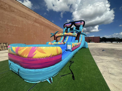 Outdoor view of Island Flow hybrid water slide with sunglasses design, displaying dual lanes, palm trees, and extended splash pool on artificial turf.