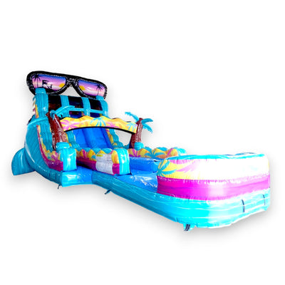 Large tropical-themed inflatable water slide with sunglasses design on top, featuring dual lanes, palm tree decorations, and a colorful splash pool at the base.