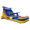 Large inflatable water slide with tropical theme, featuring three blue sliding lanes, yellow accents, palm tree decorations, and a colorful splash pool area, set up in an indoor warehouse with metal roofing and other inflatables visible.