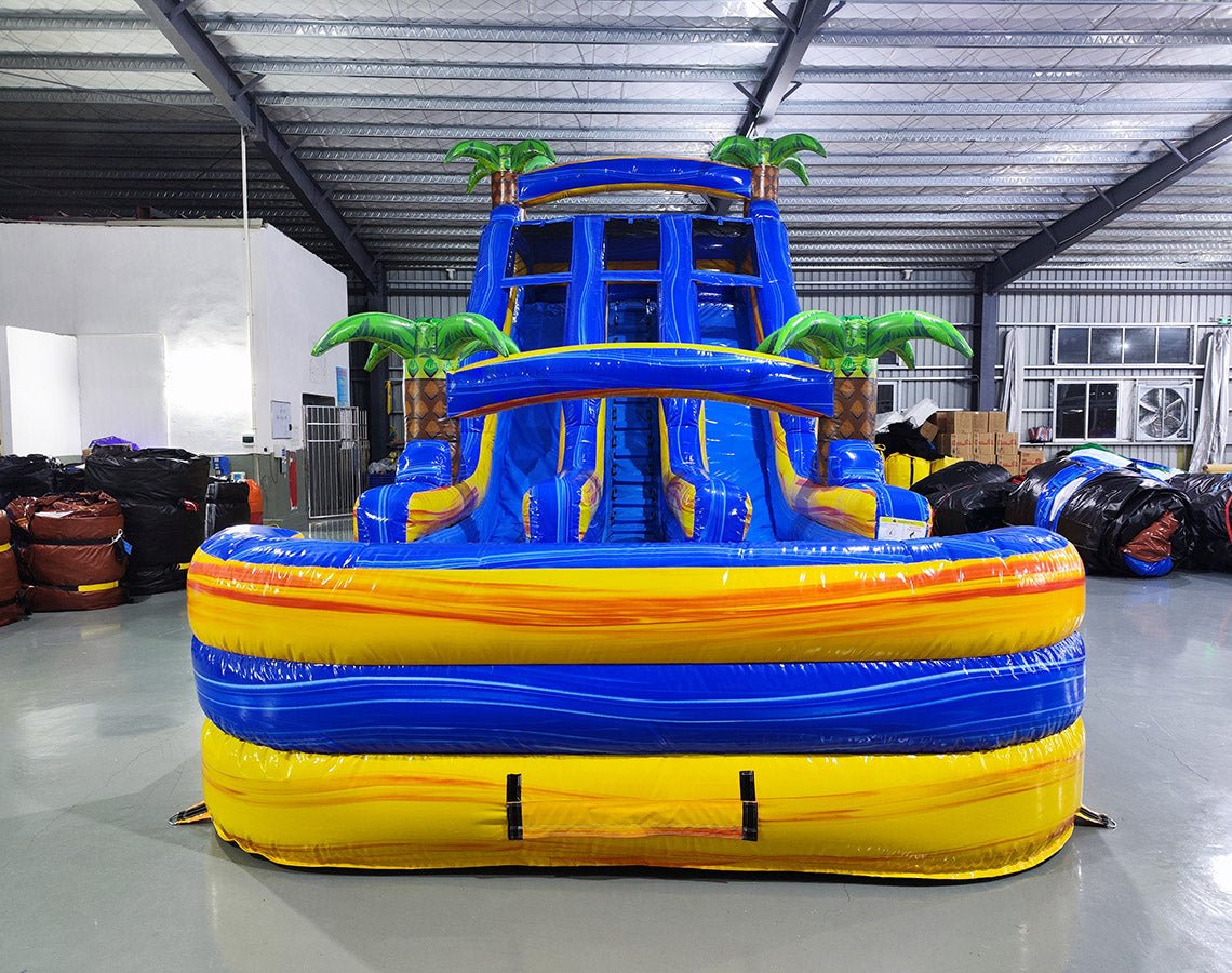 Front view of 18ft Lava Falls Center Climb water slide showing vibrant blue and yellow color scheme, three sliding lanes, inflatable palm trees, and a large splash pool area, displayed in a spacious indoor facility with other equipment visible.