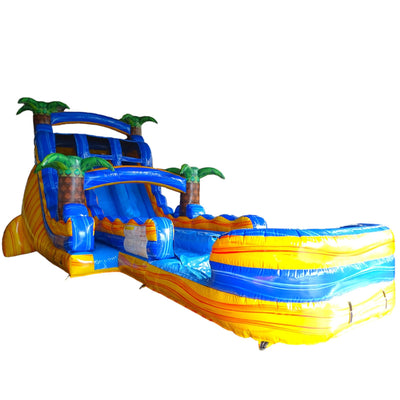 Large tropical-themed inflatable water slide with vibrant colors, featuring dual lanes, palm tree decorations, and an extended splash pool with wave design in bright yellow and blue.