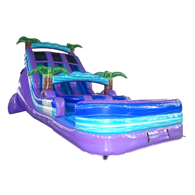 Large inflatable water slide with tropical theme, featuring purple base, blue sliding lanes, green palm tree decorations, and a colorful splash pool area, isolated on a white background.