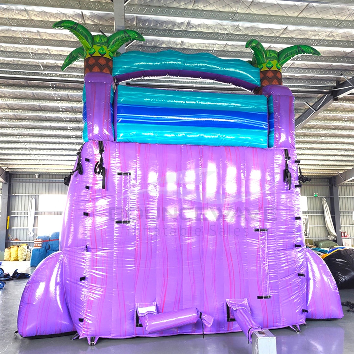 Rear view of Purple Plunge hybrid water slide showcasing tall purple structure with climbing area, safety features, and palm tree decorations on top.