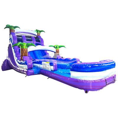 Large tropical-themed inflatable water slide featuring dual purple sliding lanes, palm tree decorations, and an extended splash pool with blue wave-like design.