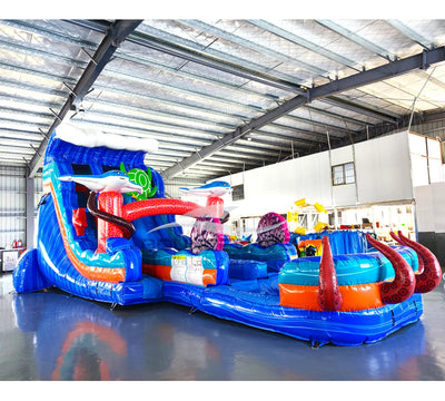 Large ocean-themed inflatable water slide with blue base, featuring dual lanes, shark and fish decorations, and an extended splash pool with octopus tentacles.