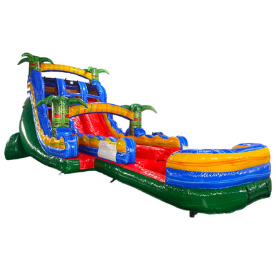 Large tropical-themed inflatable water slide with vibrant colors, featuring dual lanes, palm tree decorations, and an extended splash pool in indoor warehouse setting.