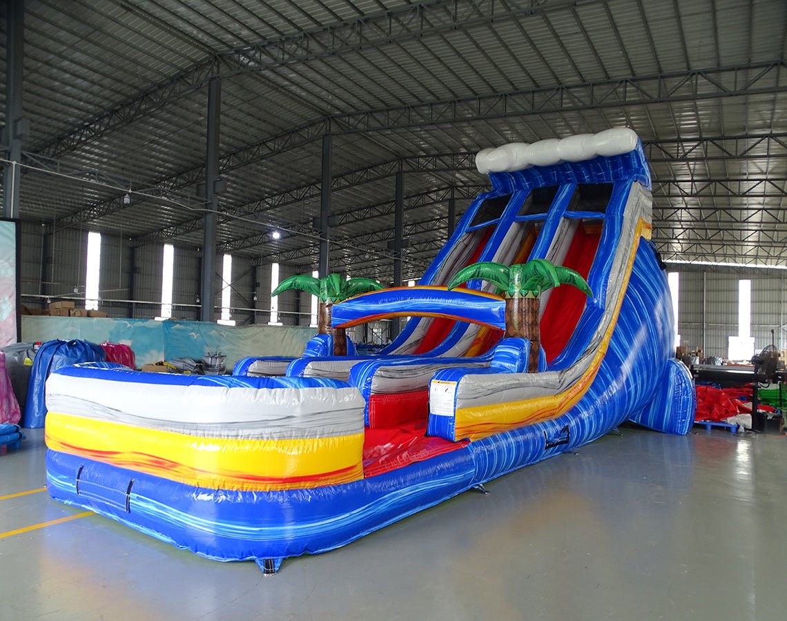 Angled view of 18ft Rip Curl Center Climb water slide featuring blue sliding lanes, inflatable palm trees, central climbing structure, and a spacious splash pool with yellow and white accents, displayed in a large indoor facility.