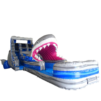 Large inflatable water slide featuring a giant shark head with open jaws, dual blue sliding lanes, and an extended splash pool with wave design and inflatable barriers.