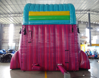 Rear view of Summer Luau inflatable water slide, displaying tall pink structure with climbing area, safety features, and tropical-themed top section with colorful stripes.