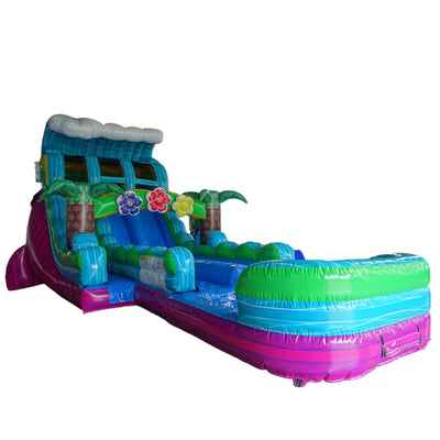 Large tropical-themed inflatable water slide featuring palm tree decorations, dual blue sliding lanes, colorful flower accents, and an extended splash pool with vibrant blue and pink base.