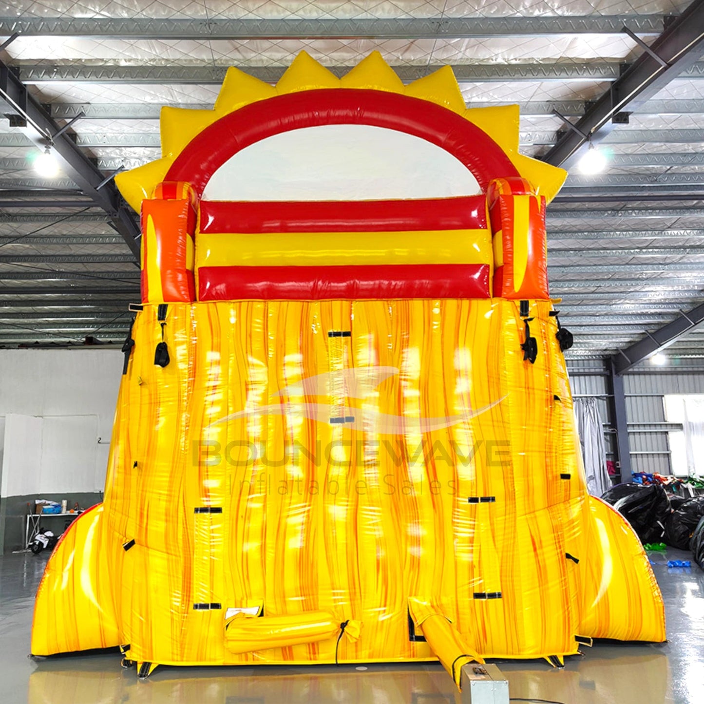 Rear view of Summer Sizzler hybrid water slide showcasing tall yellow structure with climbing area, safety features, and sun-shaped top with red accents.