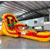 Large tropical-themed inflatable water slide featuring sun design on top, dual sliding lanes, palm tree decorations, and an extended splash pool with red and yellow colors.