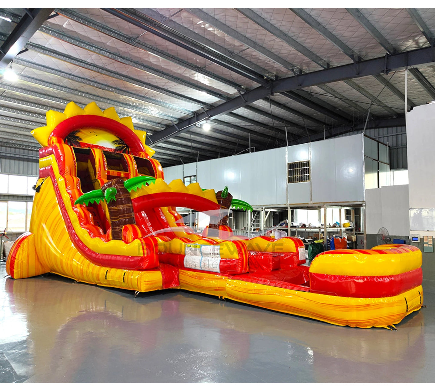 Large tropical-themed inflatable water slide featuring sun design on top, dual sliding lanes, palm tree decorations, and an extended splash pool with red and yellow colors.