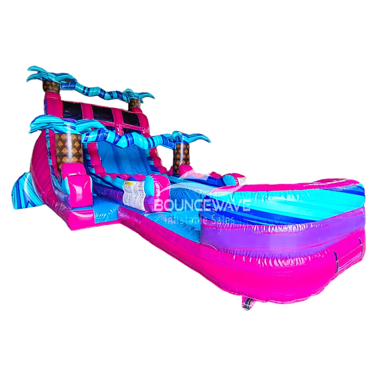 Large tropical-themed inflatable water slide featuring vibrant pink and blue colors, dual sliding lanes, palm tree decorations, and an extended splash pool with wave-like design.