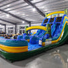 Side view of 18ft Tiki Shot Center Climb water slide showing vibrant blue, yellow, and green colors, tiki decorations, and a large splash pool area, displayed in a spacious indoor facility with metal roofing.