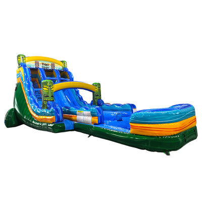 Large tropical-themed inflatable water slide featuring tiki mask decorations, dual blue sliding lanes, palm tree accents, and an extended splash pool with green base and colorful stripes.