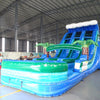 Side angle view of 18ft Trop Wave Center Climb water slide showing blue sliding lanes, inflatable palm trees, and a large splash pool area. The slide is set up in an indoor facility with other inflatables visible in the background.