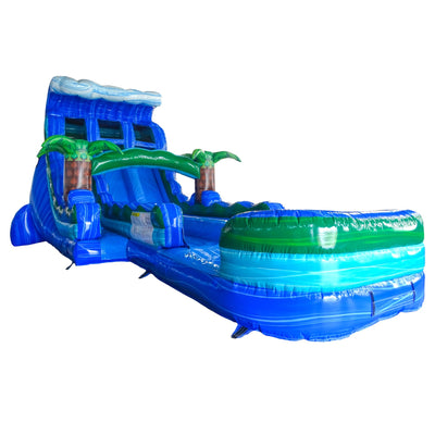 Large tropical-themed inflatable water slide featuring blue wave design, dual sliding lanes, palm tree decorations, and an extended splash pool with green and blue colors.