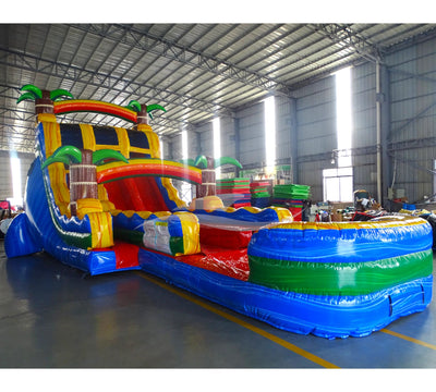 Large tropical-themed inflatable water slide featuring palm tree decorations, dual sliding lanes, and an extended splash pool with vibrant blue, yellow, and red colors.