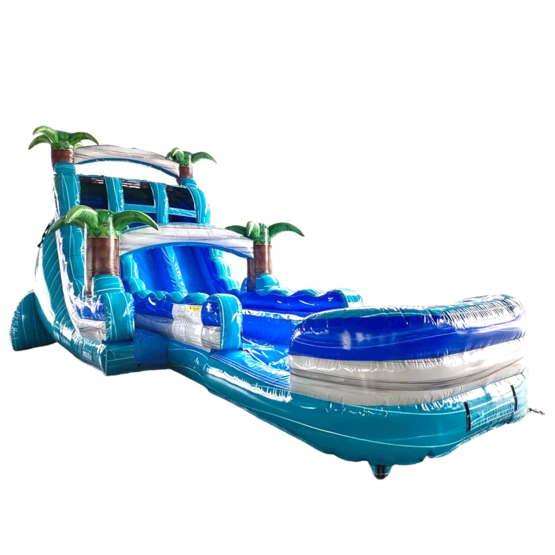 Large inflatable water slide with tropical theme, featuring blue sliding lanes, palm tree decorations, and a spacious splash pool area. The slide combines open and enclosed sections, set up in an indoor warehouse with metal roofing visible.