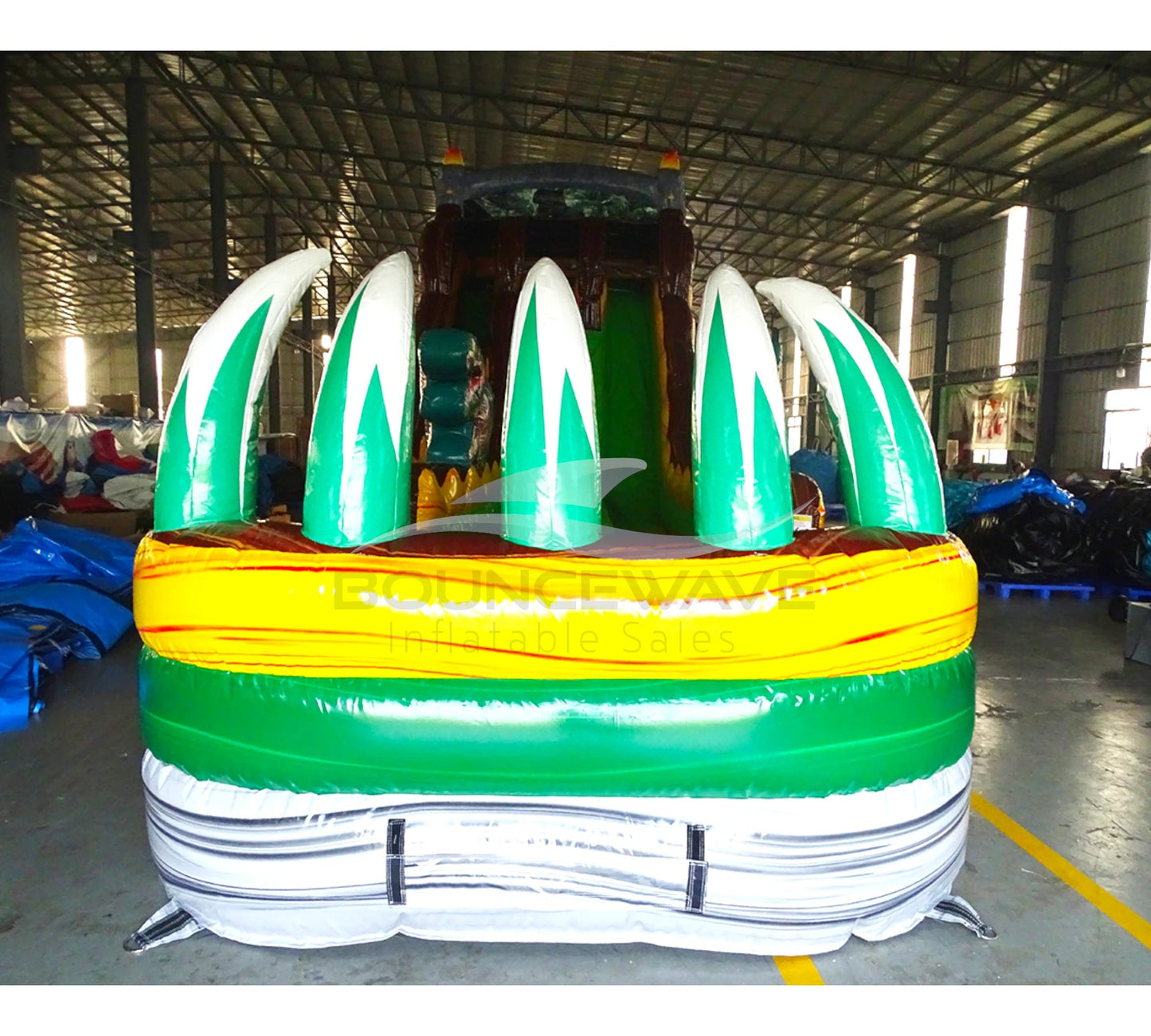 Front view of the 20ft Dino Dive Hybrid DL inflatable water slide, showcasing its green sliding lanes, T-Rex decorations, and spacious splash pool with "BOUNCEWAVE" branding. The slide combines open and tube slide elements, set up in an indoor warehouse.