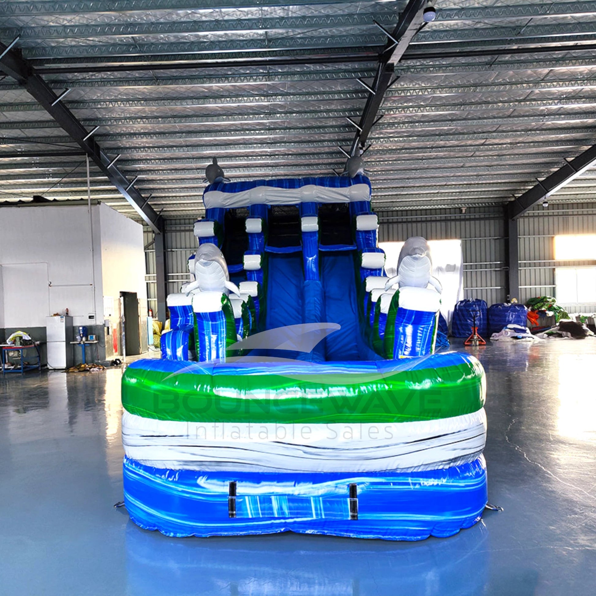 Front view of the 20ft Dolphin Dive Hybrid DL inflatable water slide, showcasing its blue sliding lanes, dolphin decorations, and spacious splash pool with "BOUNCEWAVE Inflatable Sales" branding. The slide combines open and tube slide elements, set up in an indoor warehouse.