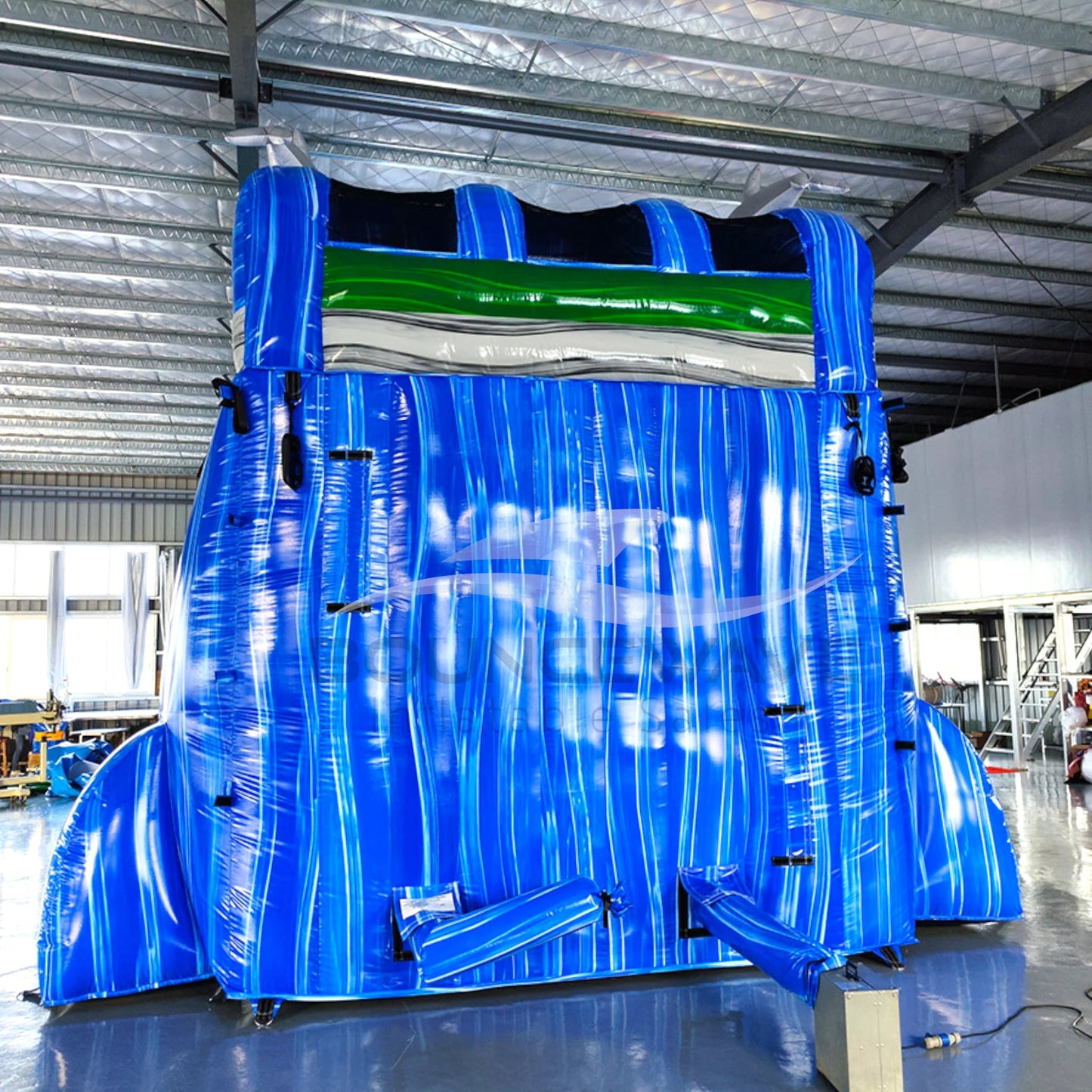 Rear view of 20ft Dolphin Dive Hybrid DL water slide showing blue color scheme, inflatable dolphin figures on top, and enclosed tube slide sections. The slide is set up in an indoor facility with white walls and metal roofing visible.