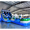 Angled view of 20ft Dolphin Dive Hybrid DL water slide featuring blue color scheme, dolphin figures, and a large splash pool area. The slide is set up in an indoor warehouse with metal roofing and other equipment visible in the background.