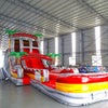 Front angle view of the 20ft Fire Island Hybrid DL inflatable water slide, showcasing its red, yellow, and white color scheme, palm tree decorations, and spacious splash pool. The slide combines open and tube slide elements, set up in an indoor warehouse with other inflatables visible.