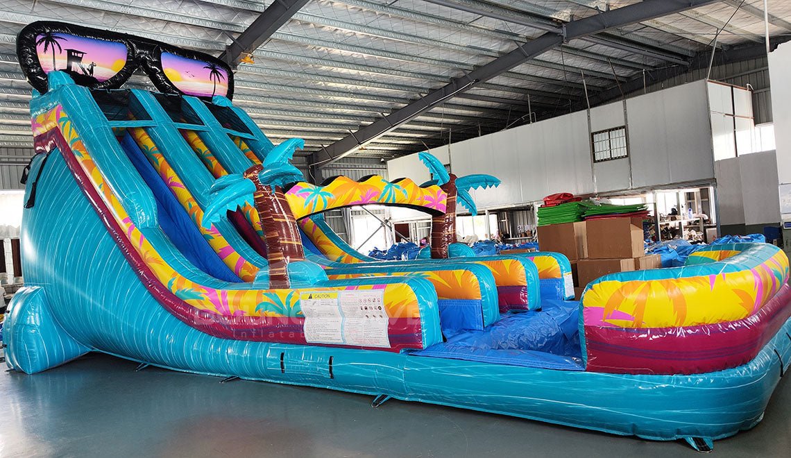 20ft Island Flow Dual Lane Center Climb Inflatable Water Slide featuring tropical theme, dual slides, sunglasses-shaped top, and palm tree decorations in warehouse setting
