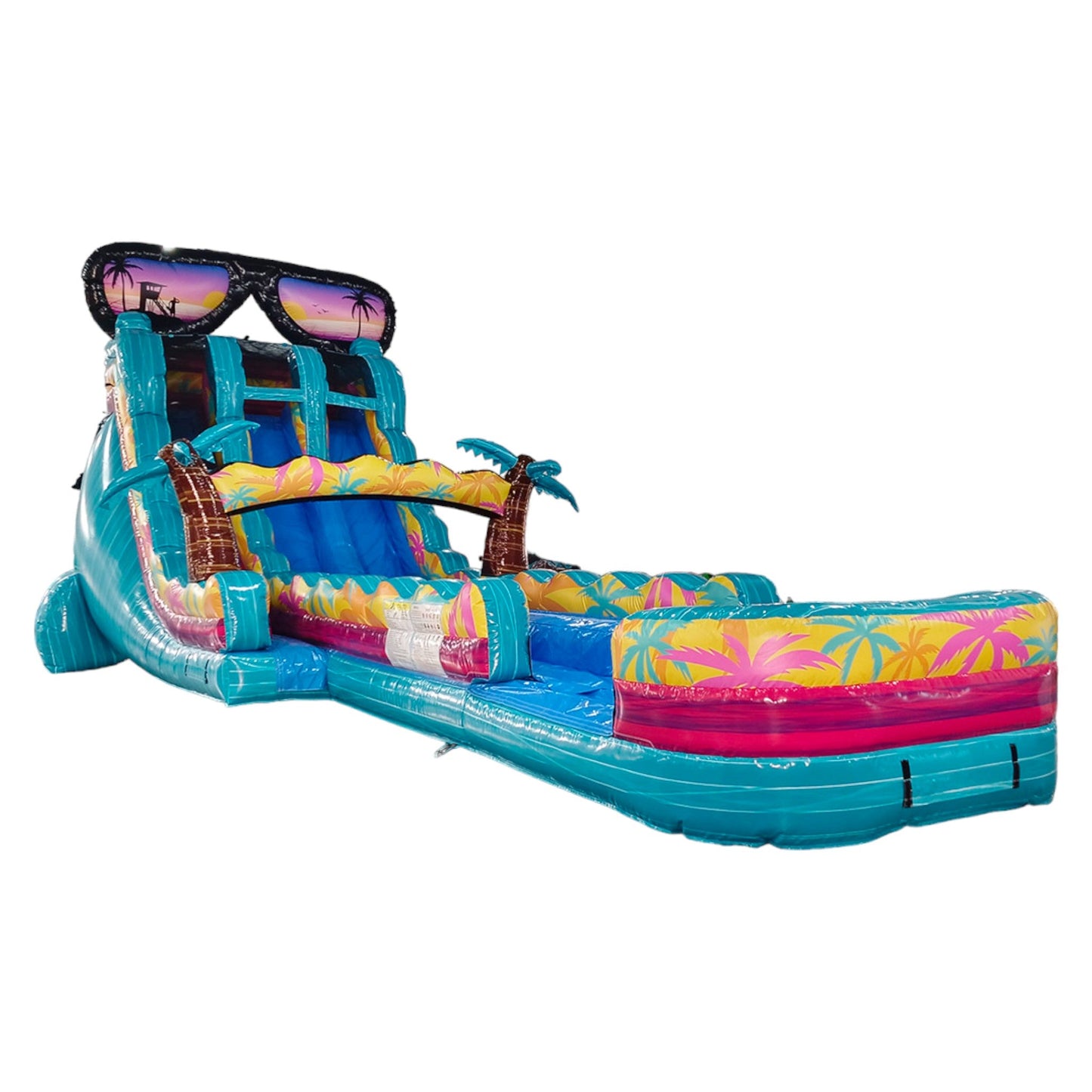 Large inflatable water slide with tropical theme, featuring turquoise sliding lanes, palm tree decorations, and a giant sunglasses topper. The slide has a spacious splash pool area with colorful palm tree designs and is set up in an indoor warehouse.