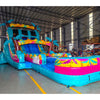 Front angle view of the 20ft Island Flow Palms Hybrid DL inflatable water slide, showcasing its turquoise sliding lanes, palm tree decorations, and spacious splash pool with colorful tropical designs. The slide is set up in an indoor warehouse with other equipment and inflatables visible.