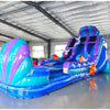 Angled view of 20ft Mermaid's Cove Hybrid DL water slide featuring blue, purple, and turquoise color scheme, shell-shaped design, mermaid figures, and a large splash pool area. The slide is set up in an indoor facility with metal roofing and other inflatables visible in the background.