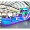 Large inflatable water slide with tropical theme, featuring vibrant purple and blue colors, palm tree decorations, and a spacious splash pool area. The slide combines open and enclosed sections, set up in an indoor warehouse with metal roofing visible.