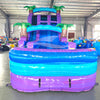 Front view of 20ft Purple Plunge Hybrid DL water slide featuring purple and blue colors, inflatable palm trees, and a large splash pool area. The slide is set up in an indoor facility with metal roofing and other inflatable products visible in the background.