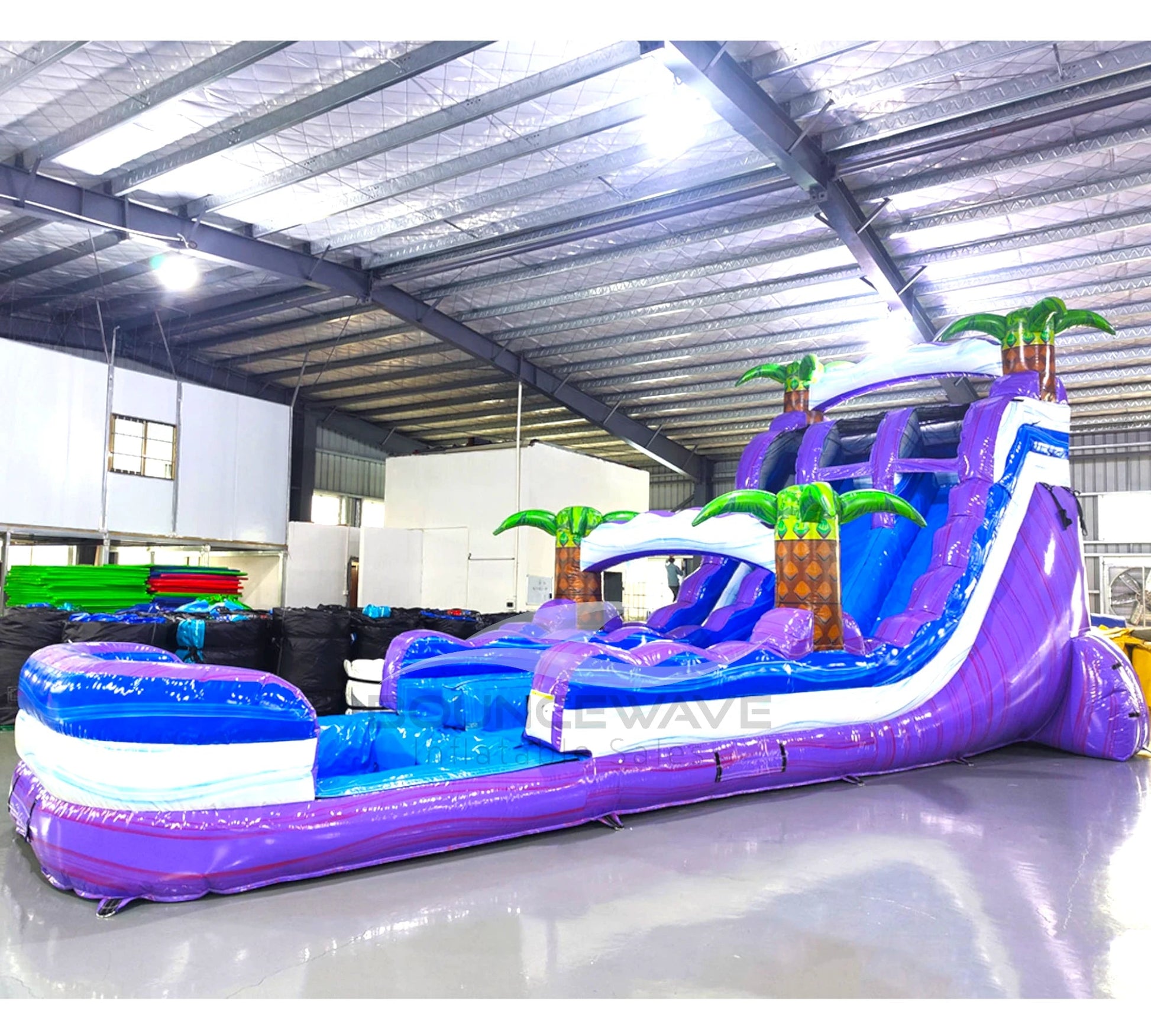 Side view of 20ft Purple Thunder Hybrid DL water slide showing bright purple and blue design, inflatable palm trees, and a large splash pool area. The slide features both open and enclosed sliding sections, displayed against a white background.