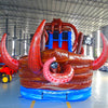 Large inflatable water slide with pirate ship theme, featuring red and brown colors, octopus tentacles, and a skull and crossbones flag. The slide has multiple lanes, a spacious splash pool area, and combines open and enclosed sections, set up in an indoor warehouse.