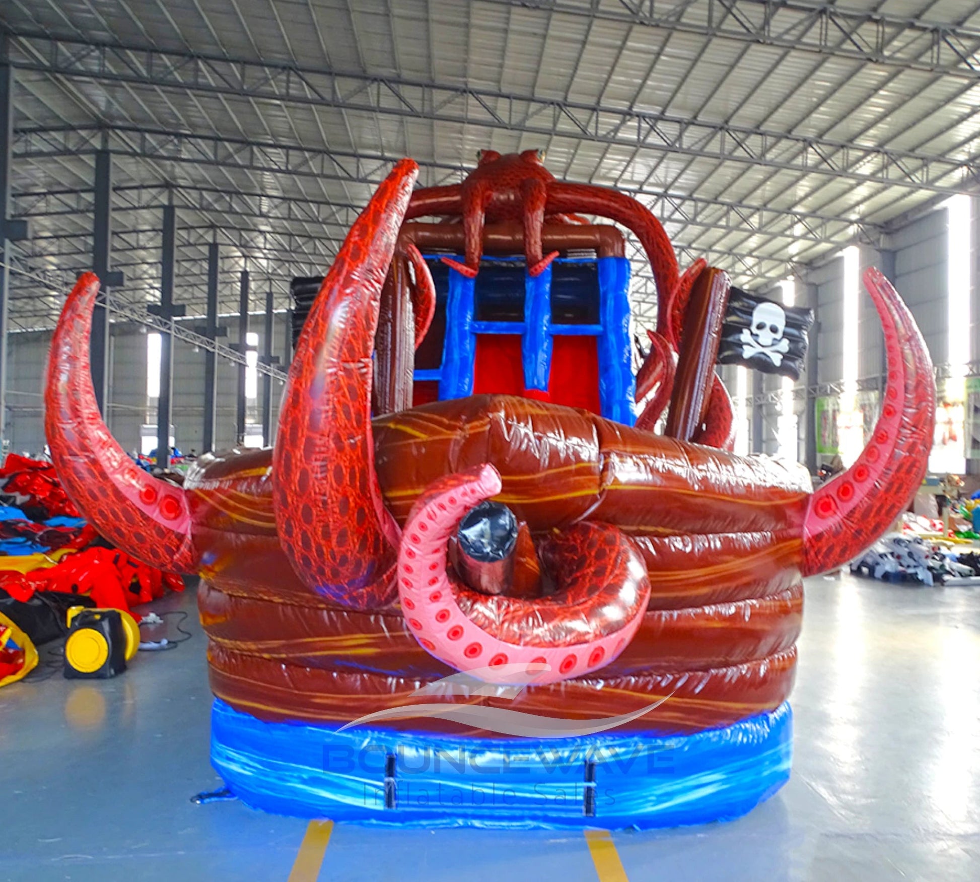 Large inflatable water slide with pirate ship theme, featuring red and brown colors, octopus tentacles, and a skull and crossbones flag. The slide has multiple lanes, a spacious splash pool area, and combines open and enclosed sections, set up in an indoor warehouse.