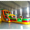 Side view of 20ft Tropical Inferno Hybrid DL water slide showing bright red, yellow, and green design, inflatable palm trees, and a large splash pool area. The slide features both open and enclosed sliding sections, displayed in an indoor facility with other inflatables visible.