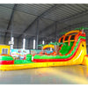 Angled view of the 20ft Tropical Inferno Hybrid DL inflatable water slide, showcasing its red, yellow, and green sliding lanes, palm tree decorations, and spacious splash pool. The slide combines open and tube slide elements, set up in an indoor warehouse with other equipment visible.