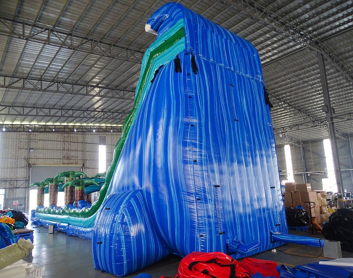 24ft Trop Wave DL 2pc Commercial Water Slide with Inflatable Slip & Slide side view showcasing tall blue slide, inflatable palm trees, and long slip and slide attachment