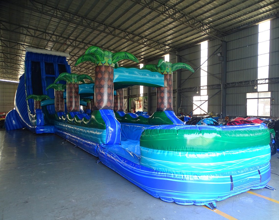 24ft Trop Wave DL 2pc Commercial Water Slide with Inflatable Slip & Slide front view highlighting vibrant colors, palm tree decorations, and extended blue water slide
