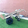 4-Wheel Heavy Duty Hand Truck Dolly with Brake featuring tan metal frame, large pneumatic tires, and brake mechanism for secure stopping on green turf
