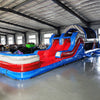 Side view of 46ft Baja Commercial Hybrid Inflatable Obstacle Course in a large indoor warehouse. The inflatable features a red, white, and blue color scheme with multiple obstacles including slides, tunnels, and climbing walls. The course stretches across the warehouse floor, showcasing its length. Metal roofing, support beams, and windows are visible in the background.