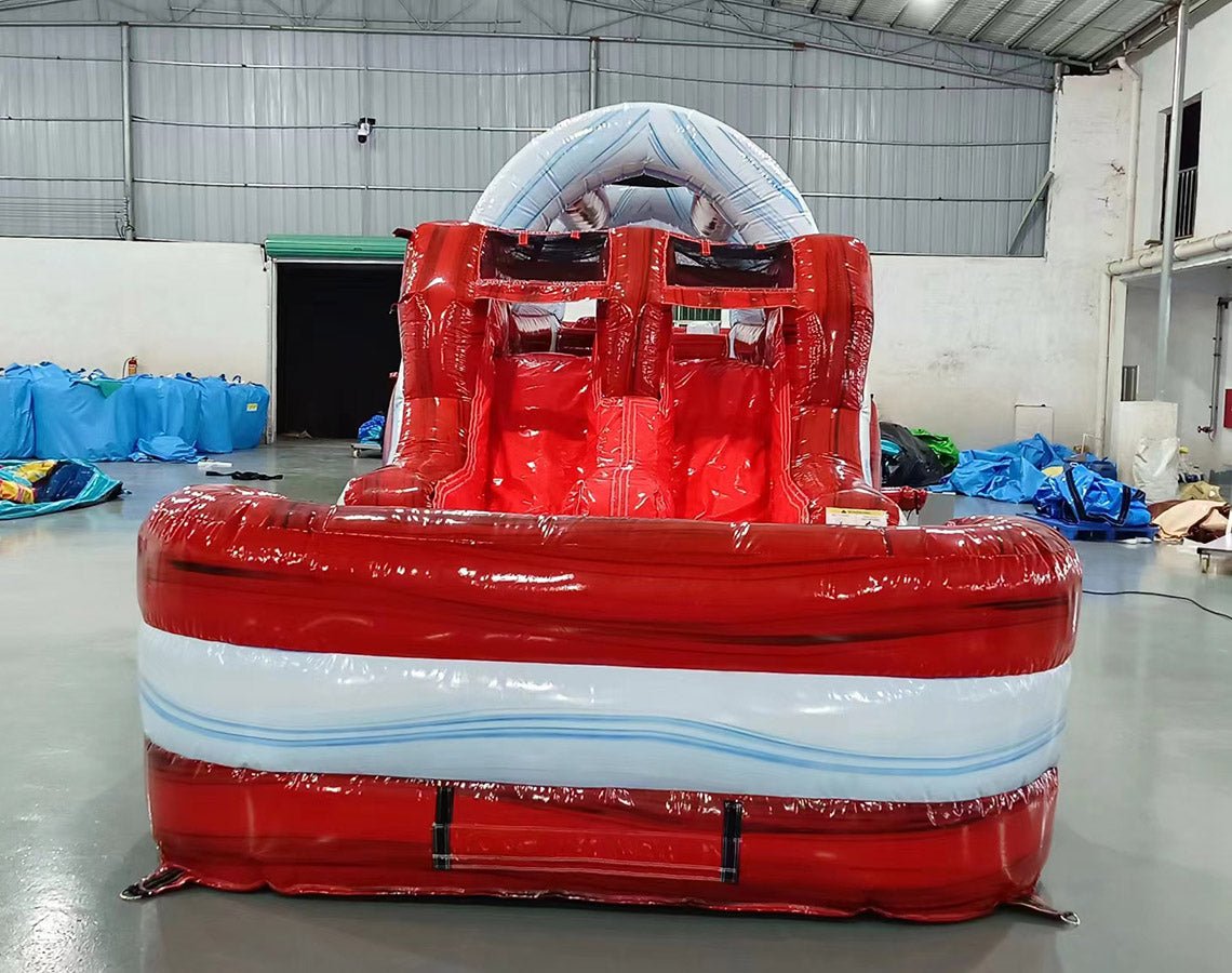 Front-angle view of 46ft Crimson Bay Commercial Hybrid Inflatable Obstacle Course showing its full length. The structure features a red base with blue accents, multiple climbing walls, slides, and various obstacles. Set up in a warehouse with metal roofing and bright lighting, showcasing its scale and commercial application.