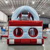 Rear view of 46ft Crimson Bay Commercial Hybrid Inflatable Obstacle Course set up in a large indoor warehouse. The inflatable features a red base with blue accents, multiple climbing walls, slides, and obstacles. Metal roofing and various other inflatable products are visible in the background.