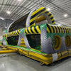 Wide-angle view of 46ft Hazardous Commercial Hybrid Inflatable Obstacle Course set up in a spacious warehouse. The inflatable displays a yellow and black hazard stripe design with multiple obstacles, tunnels, and climbing areas. Other inflatable products and warehouse equipment are visible, showcasing its size and commercial setting.