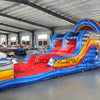 Wide-angle view of 46ft Rip Curl Commercial Hybrid Inflatable Obstacle Course set up in a spacious warehouse. The inflatable displays a blue, yellow, and red color scheme with multiple obstacles, including a large red slide, tunnels, and arches. Various other inflatable products and warehouse equipment are visible, demonstrating its size and commercial setting.