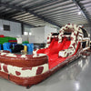 Side view of 46ft Rodeo Rush Commercial Hybrid Inflatable Obstacle Course showing its full length. The inflatable features a cow-print design with dual red slides emerging from the structure. A large inflatable cow figure arches over the top. Various inflatable obstacles and colorful storage bags are visible in the warehouse setting.