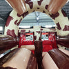 Interior view of 46ft Rodeo Rush Commercial Hybrid Inflatable Obstacle Course showing dual lanes with red inflatable obstacles. The structure features a cow-print design on the walls and ceiling, with a central brown divider. Red inflatable cylinders and platforms are visible as part of the obstacle course.